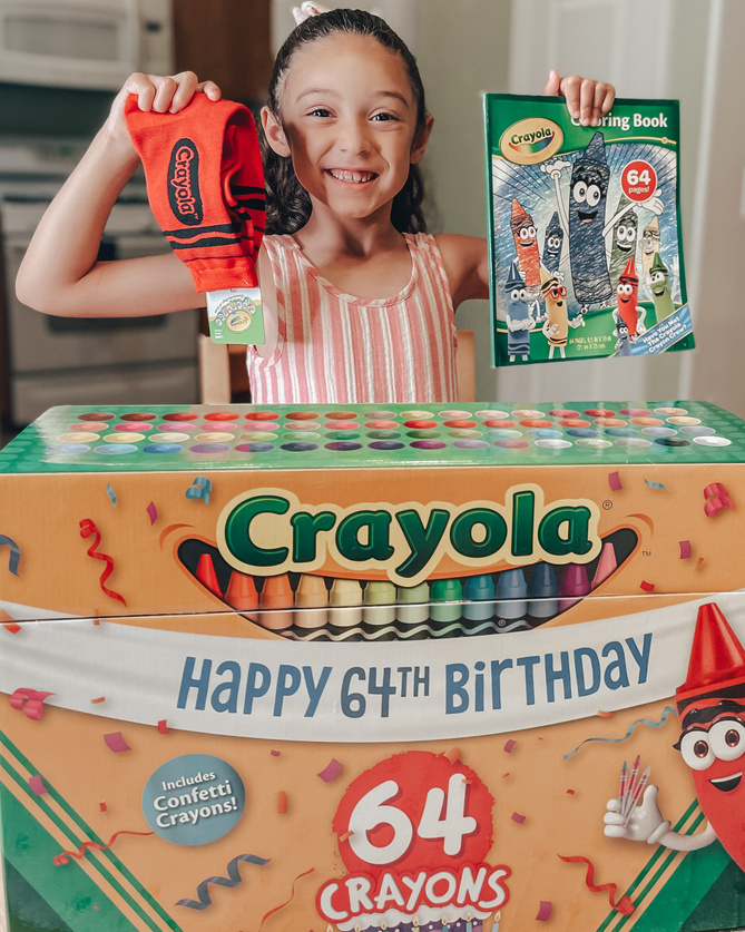 user generated content photo for Crayola's 64th Birthday. Little girl holding up items from large Crayola crayons box